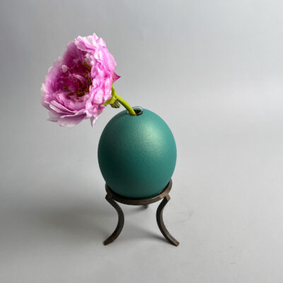 Ostrich egg in petrol on metal stand with flower